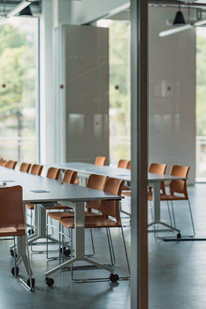 Spacious office interior featuring modern tables and orange chairs with large windows.